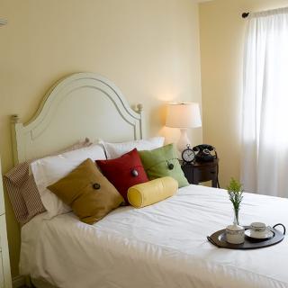 A cozy bedroom with a neatly made bed adorned with colorful pillows and a bedside lamp.