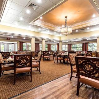 A spacious and elegantly designed dining room with ornate chairs and tables, featuring warm lighting and a carpeted floor.