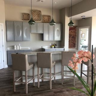 A modern kitchen with gray cabinets and a sleek countertop, accented by pendant lights and bar stools.