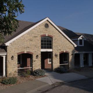 A stone-exterior residential building with a prominent entrance and windows, set against a clear sky.