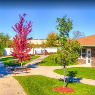 A peaceful park scene with vibrant autumn trees, a winding walkway, and a bench near a small building.
