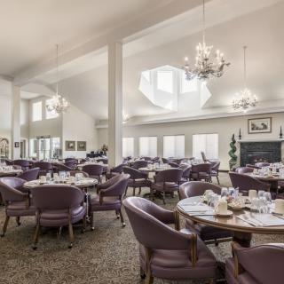 An elegant dining room with chandeliers, set tables, and comfortable seating.