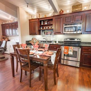 A modern kitchen and dining area featuring wooden furniture, stainless steel appliances, and bright ambient lighting.