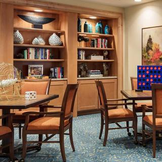 A cozy library area with wooden bookshelves, decorated with various items and a table with chairs arranged for seating.