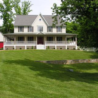 A large house with a spacious porch and a well-maintained lawn, surrounded by trees.