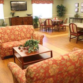 A cozy living room with floral sofas, a coffee table, and a dining area in the background.