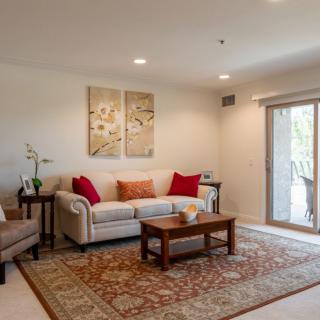 A cozy living room with a beige sofa, colorful cushions, and a wooden coffee table, adorned with artwork and an indoor plant.