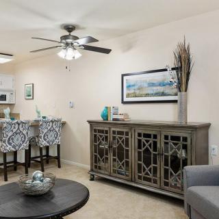 A modern living room with stylish furniture and home decor, featuring a ceiling fan and elegant bar stools overlooking the kitchen.
