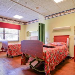 A hospital room featuring two patient beds with floral bedspreads and a curtain divider.