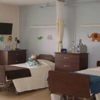 A hospital room with multiple beds and cheerful wall decorations.