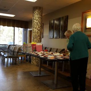 Senior citizens enjoying a community gathering in the lobby with refreshments on display.