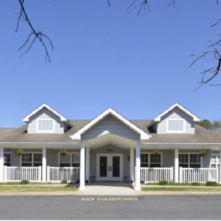 A symmetrical single-story residential building with a pitched roof and a front porch under a clear blue sky.
