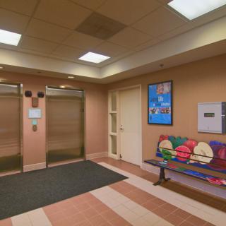 A modern lobby area featuring two elevators, a colorful bench, and wall art.