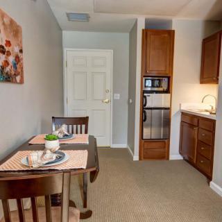 A cozy kitchenette and dining area featuring a small table set for two, wooden cabinets, a microwave, and a sink.