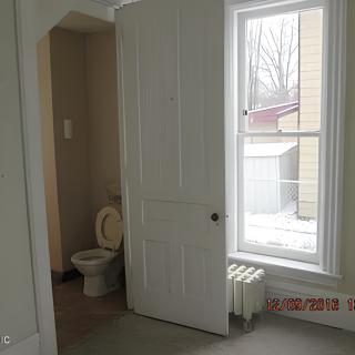 A room with a partially open door revealing a toilet, next to a large window with an outside view.