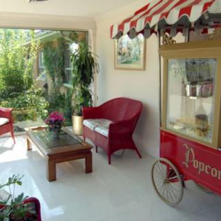 A cozy indoor space featuring a popcorn machine, red chairs, a coffee table, and lush plants with a garden view.