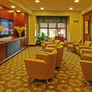 A comfortable lounge area with several chairs arranged facing a television, featuring warm lighting and patterned carpet.