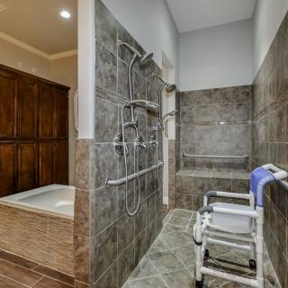 A modern, accessible bathroom featuring a walk-in shower with grab bars and a shower chair.