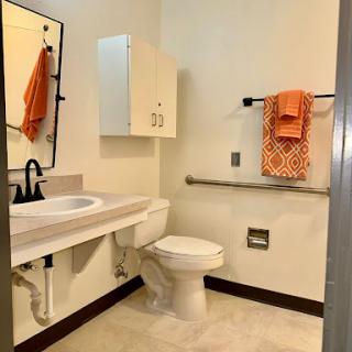 A clean and accessible bathroom featuring a toilet, sink, and bright orange towels.