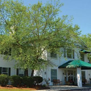 A sunny view of a building with white walls, surrounded by green trees and a clear blue sky.