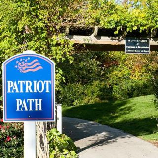A scenic trail marked by a 'Patriot Path' sign surrounded by lush greenery.