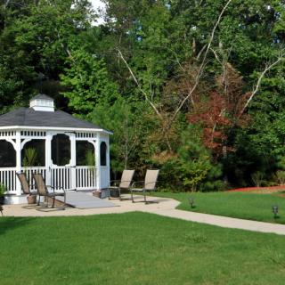 A scenic outdoor setting with a white gazebo, surrounded by lush greenery and chairs on a well-maintained lawn.