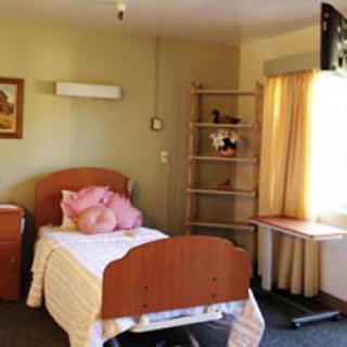 A simple hospital room featuring a bed, shelf, and window with curtains.