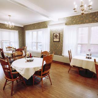 A cozy dining area featuring wooden tables and chairs, illuminated by natural light.