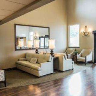 A stylish living room featuring a sofa, armchairs, and a large mirror with elegant lamps on wooden flooring.