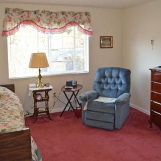A cozy bedroom with traditional decor, featuring an armchair, a lamp on a side table, and a dresser.