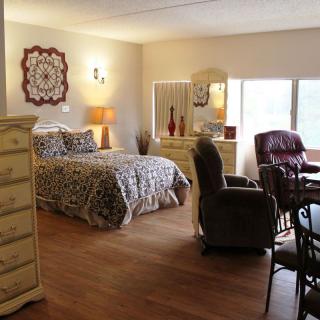 A cozy bedroom with a bed, dresser, and seating area near a window.