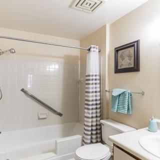 A well-organized bathroom featuring a bathtub with a striped shower curtain, a towel rack with a blue towel, and basic amenities.