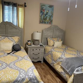 A cozy bedroom with two twin beds featuring matching yellow bedding, a central nightstand, and vibrant artwork on the wall.