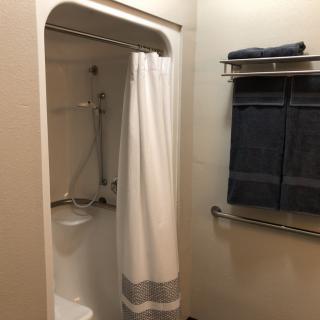 A clean bathroom featuring a shower with a white curtain and neatly folded towels on a rack.