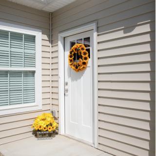 A charming entrance featuring a white door adorned with a sunflower wreath and a basket of sunflowers.