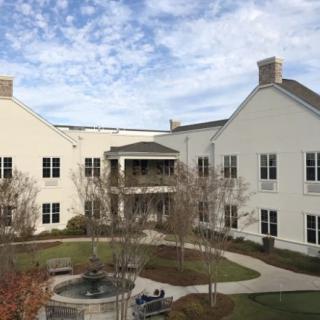 A view of a modern building with a courtyard and landscaped surroundings under a partly cloudy sky.