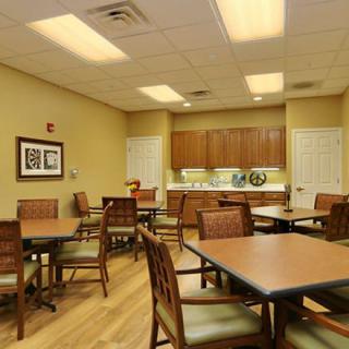 A well-lit dining area with several tables and chairs, adjacent to a kitchenette.