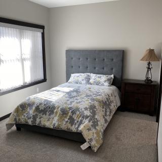 A cozy bedroom with a neatly made bed, nightstand, and lamp next to a window.