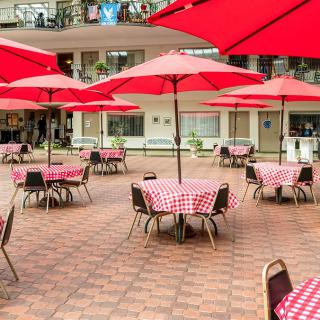 Outdoor cafe patio with red umbrellas and checkered tablecloths.