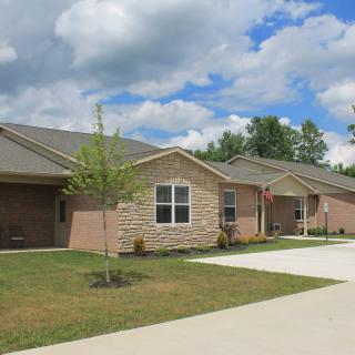 A suburban residential house with a driveway and small trees under a partly cloudy sky.