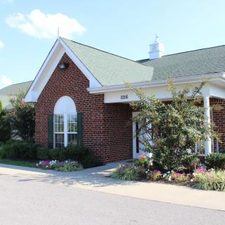 A brick building with a green roof and large windows, surrounded by landscaping.