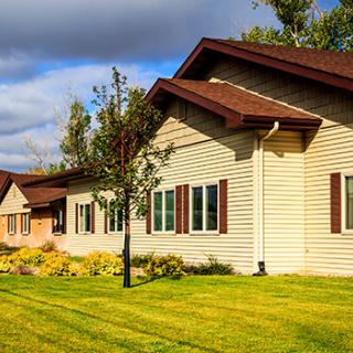 A residential building with a well-maintained lawn and trees under a cloudy sky.