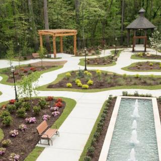 A beautifully landscaped garden featuring winding pathways, a central fountain, a gazebo, and vibrant flower beds.