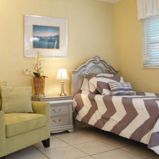 A cozy bedroom with a single bed featuring a chevron-patterned comforter, an armchair, and a nightstand adorned with a lamp.
