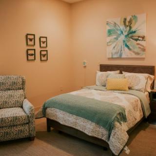A cozy bedroom with a neatly made bed and an armchair, complemented by wall art.