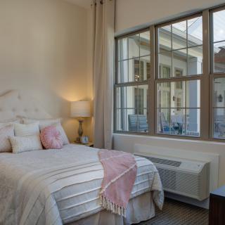 A cozy, modern bedroom with a neatly made bed, decorative pillows, and large windows allowing natural light to fill the room.