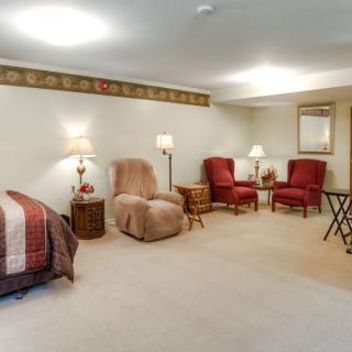 A cozy basement living area featuring recliner and red armchairs, a bed, and soft lighting from table lamps.