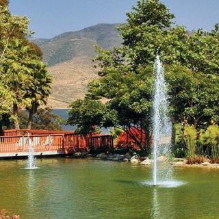 A serene pond with fountains and a red bridge set against a backdrop of mountains.