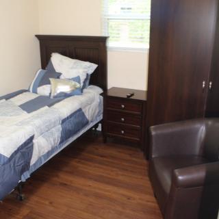 A cozy bedroom with a single bed, wooden furniture, and a comfortable chair.