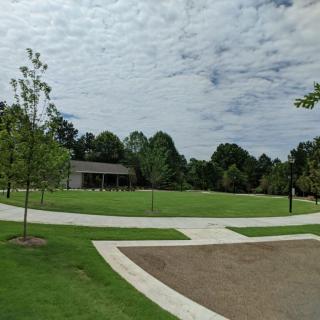 A peaceful park with a grassy field, trees, and pathways under a cloudy sky.